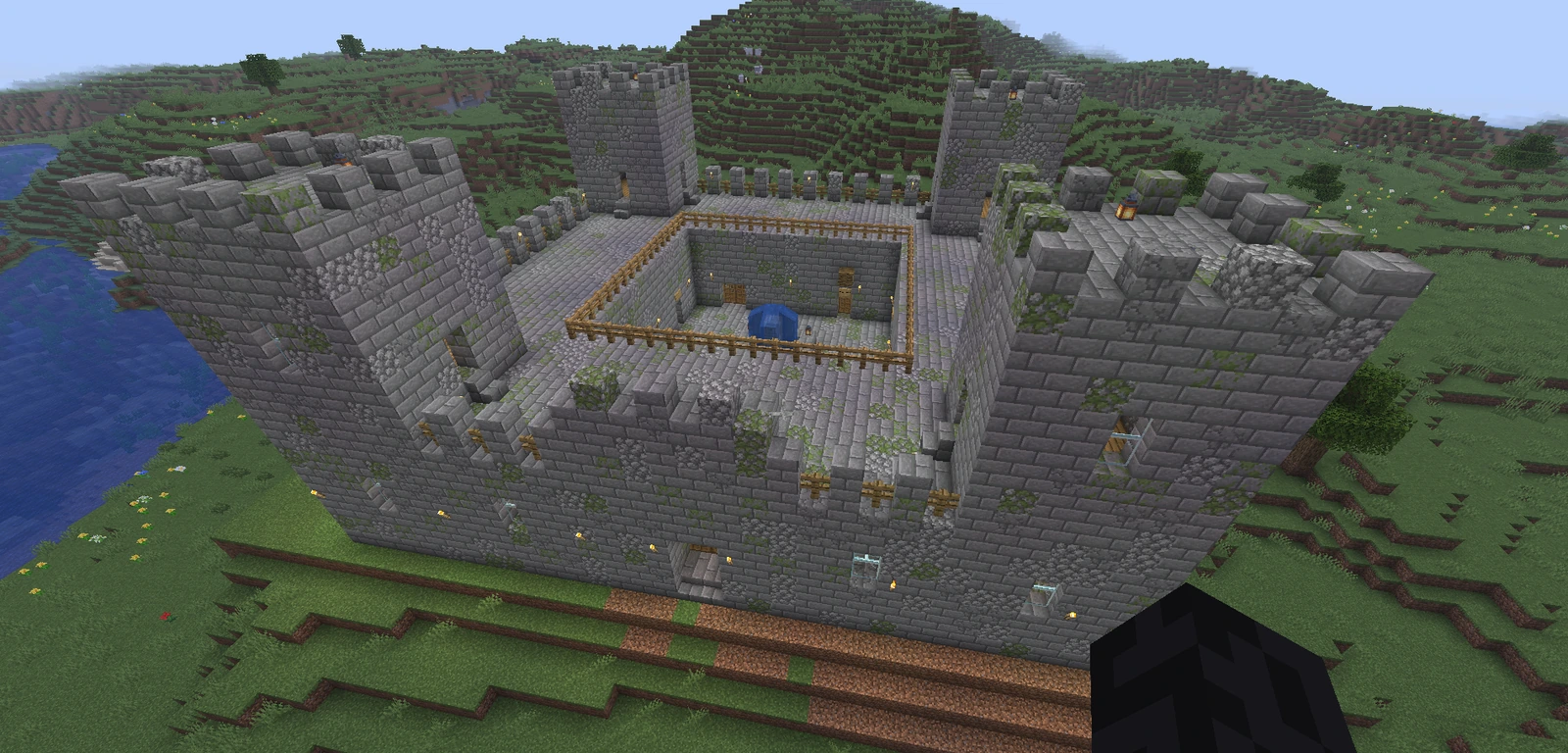 A finished dwarven fortress of grey stone with corner towers and a walled inner courtyard, beside a lake