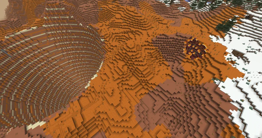 Orange and red terraced badlands seen from above, beside a snowfield